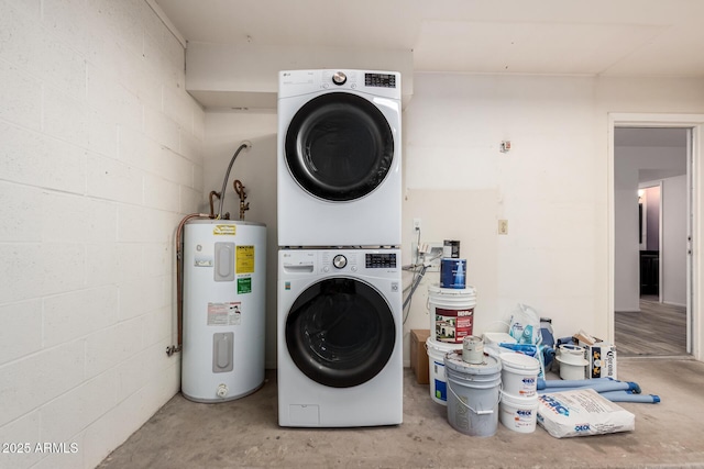 clothes washing area featuring concrete block wall, laundry area, stacked washer / drying machine, and electric water heater