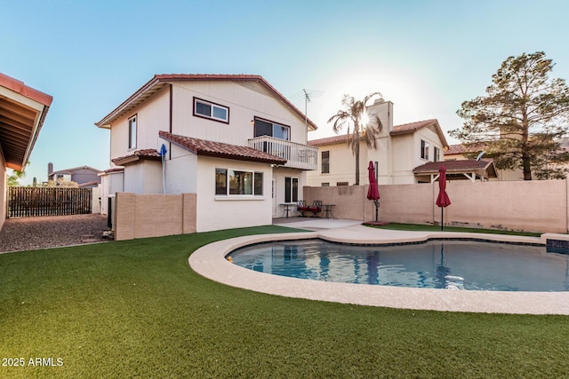 back of house featuring a tile roof, a fenced backyard, a lawn, and a balcony