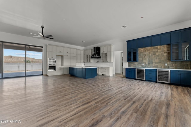 interior space featuring stainless steel double oven, beverage cooler, premium range hood, ceiling fan, and hardwood / wood-style floors