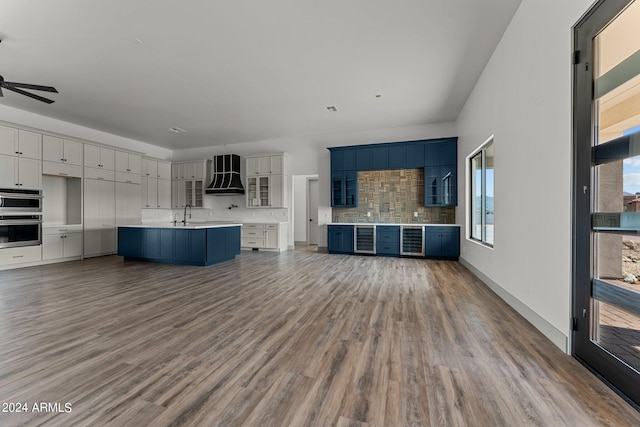 kitchen with stainless steel double oven, ceiling fan, decorative backsplash, custom range hood, and hardwood / wood-style floors