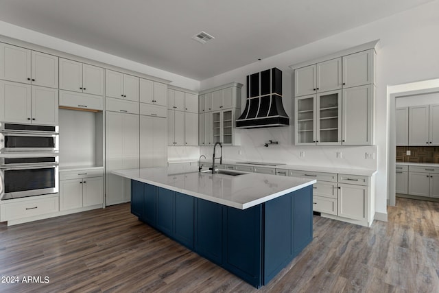 kitchen featuring decorative backsplash, custom exhaust hood, stainless steel double oven, sink, and wood-type flooring