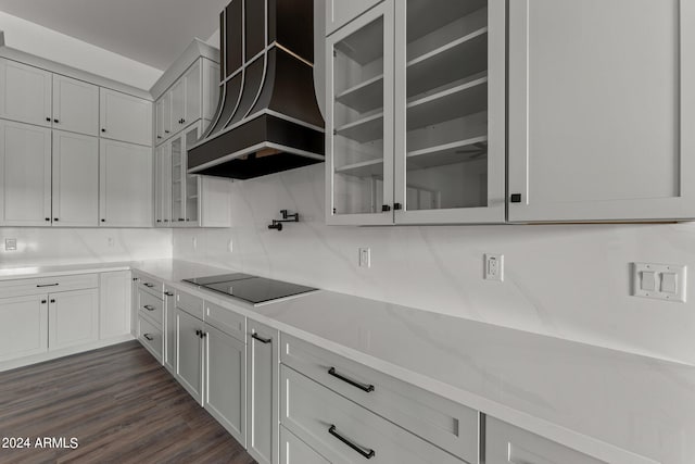 kitchen with dark wood-type flooring, black electric cooktop, custom range hood, backsplash, and white cabinetry