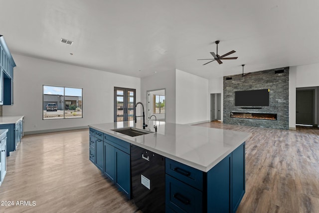 kitchen featuring blue cabinetry, sink, a stone fireplace, and light hardwood / wood-style floors