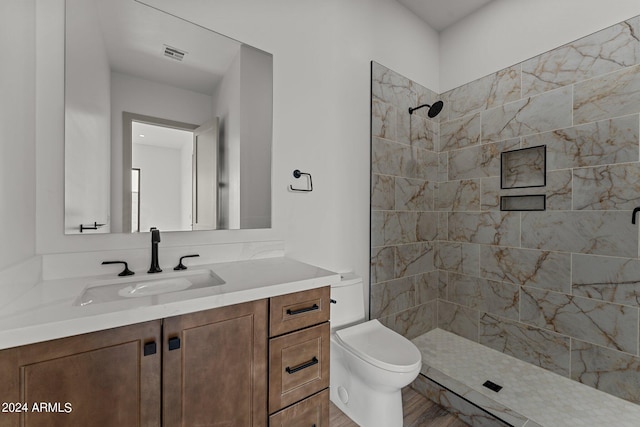 bathroom with tiled shower, toilet, vanity, and hardwood / wood-style flooring