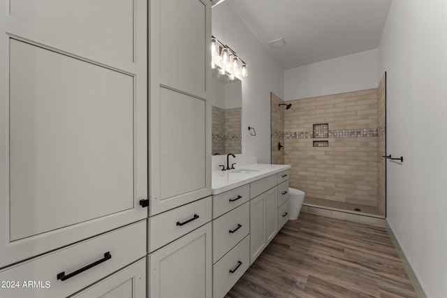 bathroom with tiled shower, hardwood / wood-style flooring, vanity, and toilet