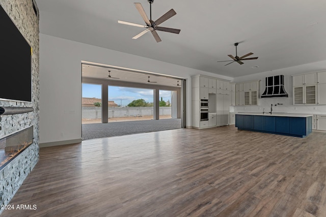 unfurnished living room featuring ceiling fan, a stone fireplace, and hardwood / wood-style flooring