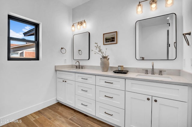 bathroom with baseboards, double vanity, and wood finished floors