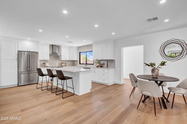 kitchen with high quality fridge, wall chimney range hood, a kitchen island, white cabinets, and light wood-type flooring