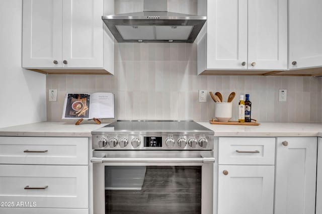 kitchen with stainless steel electric stove, wall chimney exhaust hood, white cabinetry, and decorative backsplash