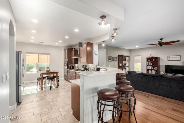 kitchen featuring appliances with stainless steel finishes, wall chimney exhaust hood, a kitchen bar, kitchen peninsula, and ceiling fan