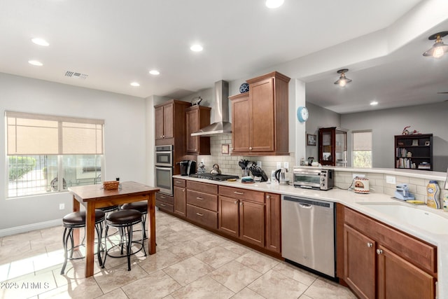 kitchen featuring backsplash, a wealth of natural light, wall chimney range hood, and appliances with stainless steel finishes