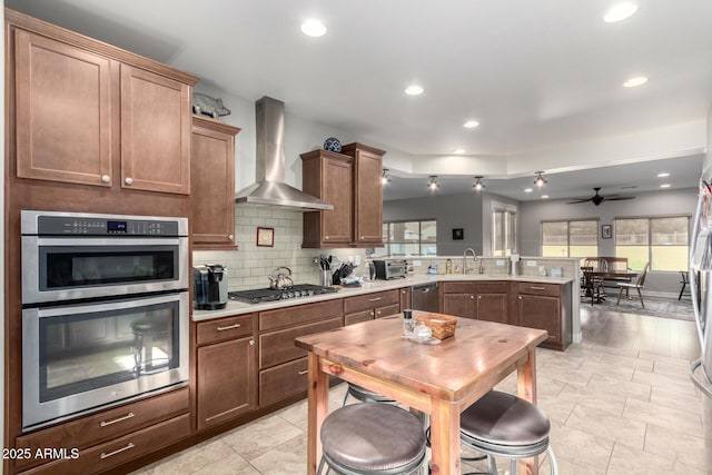 kitchen featuring wall chimney range hood, stainless steel appliances, tasteful backsplash, kitchen peninsula, and a breakfast bar area