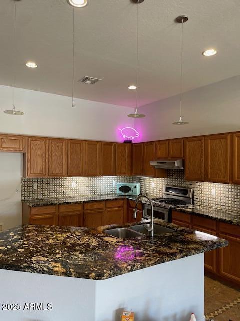 kitchen featuring sink, stainless steel gas range oven, pendant lighting, a kitchen island with sink, and decorative backsplash