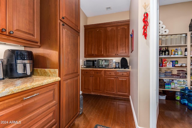 kitchen with visible vents, brown cabinets, stainless steel microwave, dark wood-style floors, and light stone countertops