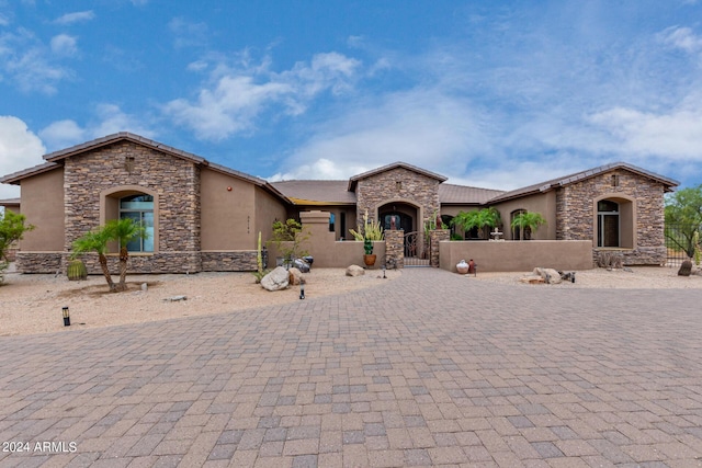 view of front of property featuring decorative driveway, a gate, a fenced front yard, and stucco siding