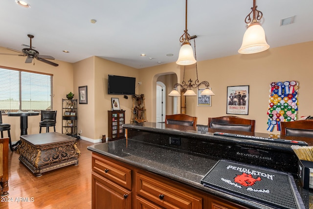 kitchen with dark stone countertops, light hardwood / wood-style flooring, hanging light fixtures, and ceiling fan