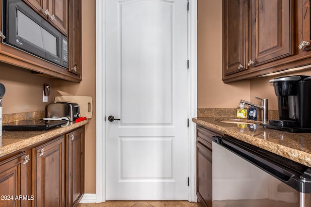 kitchen featuring light tile patterned flooring, black microwave, stainless steel dishwasher, stone countertops, and sink