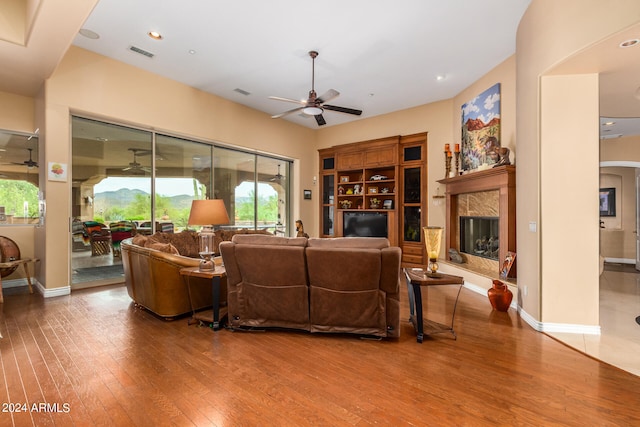 living room with a premium fireplace, ceiling fan, and wood-type flooring