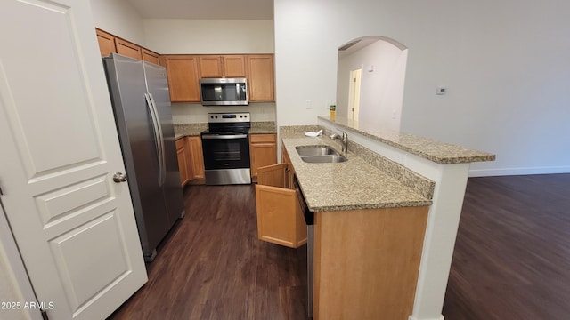 kitchen with sink, appliances with stainless steel finishes, light stone counters, dark hardwood / wood-style flooring, and kitchen peninsula