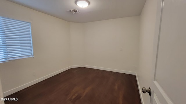 unfurnished room with visible vents, dark wood finished floors, and baseboards