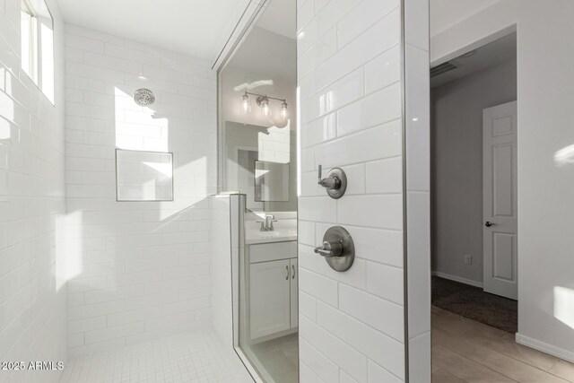 bathroom with hardwood / wood-style flooring, a tile shower, and vanity