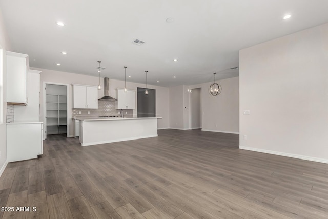 kitchen featuring a center island with sink, pendant lighting, wall chimney exhaust hood, hardwood / wood-style flooring, and white cabinets