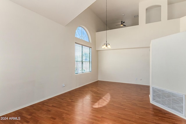 unfurnished room featuring ceiling fan with notable chandelier, high vaulted ceiling, and hardwood / wood-style flooring