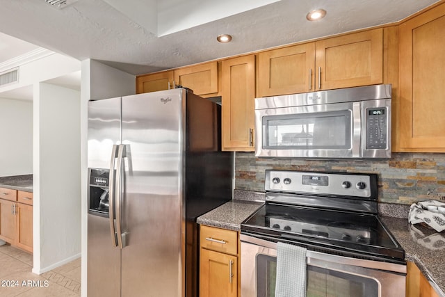 kitchen with decorative backsplash, dark stone counters, light tile patterned floors, and stainless steel appliances