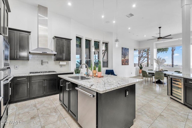 kitchen featuring visible vents, a sink, stainless steel appliances, wine cooler, and wall chimney range hood