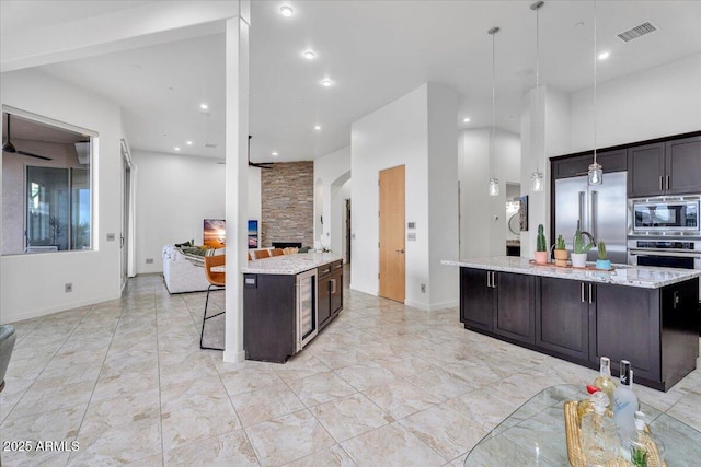 kitchen with light stone counters, a center island with sink, visible vents, dark brown cabinetry, and built in appliances