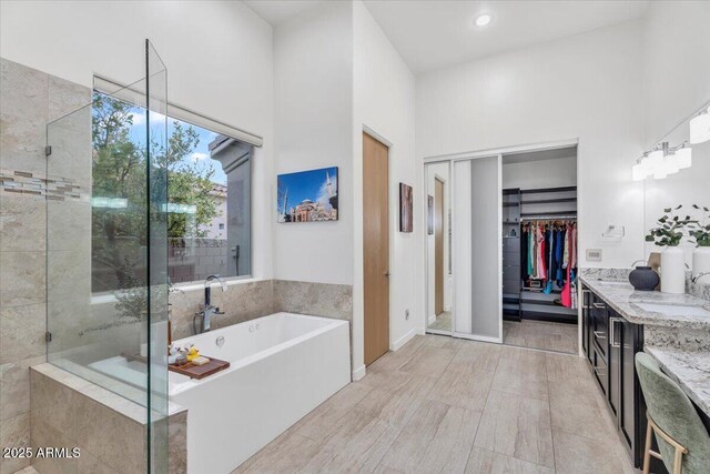 bathroom with vanity, a freestanding tub, a towering ceiling, walk in shower, and a walk in closet