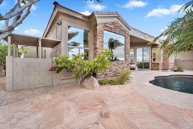 back of house with stucco siding, stone siding, a patio, and fence