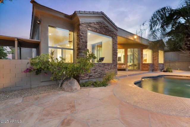 rear view of property with stone siding, stucco siding, a patio, and fence