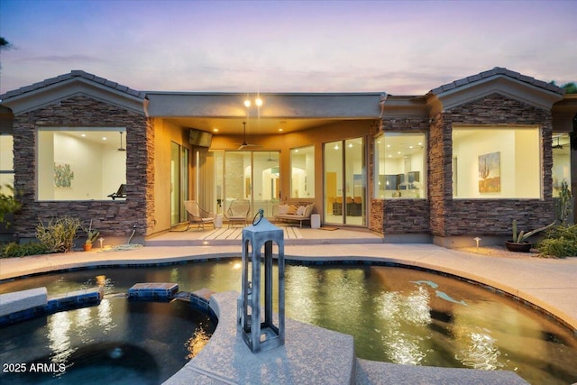 pool at dusk featuring a pool with connected hot tub and ceiling fan