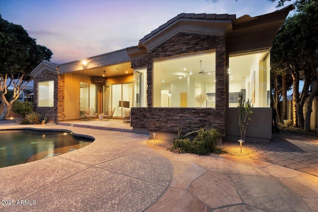 rear view of property featuring stucco siding, stone siding, a patio, and a ceiling fan