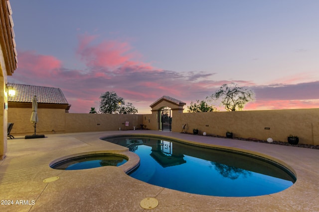 pool at dusk featuring an in ground hot tub and a patio area