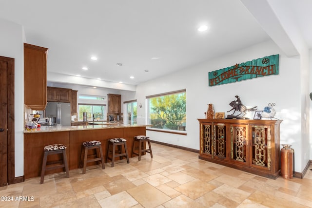 kitchen featuring kitchen peninsula, light stone countertops, stainless steel fridge, and a kitchen breakfast bar