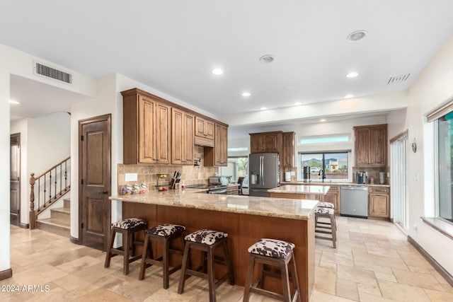 kitchen with light stone counters, stainless steel appliances, kitchen peninsula, backsplash, and a kitchen bar