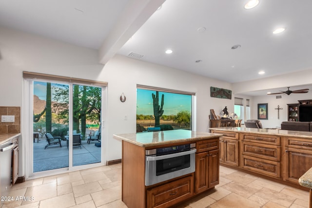 kitchen with ceiling fan, beam ceiling, stainless steel appliances, light stone countertops, and a center island