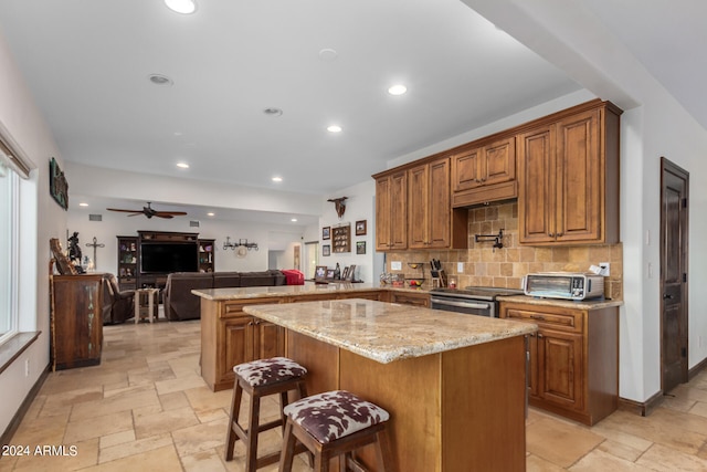 kitchen with light stone counters, kitchen peninsula, backsplash, stainless steel stove, and a breakfast bar