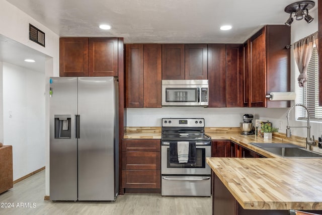 kitchen with wood counters, stainless steel appliances, sink, and light hardwood / wood-style floors