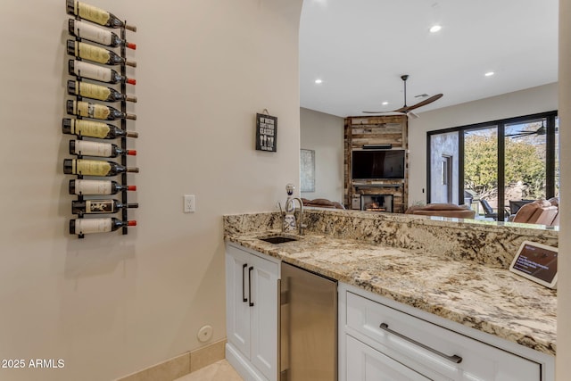 kitchen featuring sink, fridge, light stone counters, white cabinets, and a stone fireplace