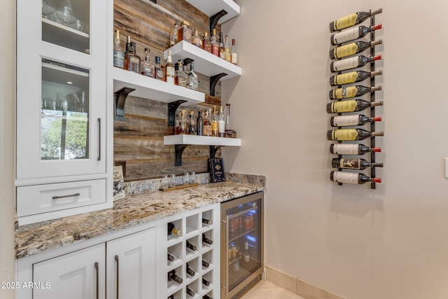 bar featuring light stone counters, light tile patterned floors, beverage cooler, and white cabinets