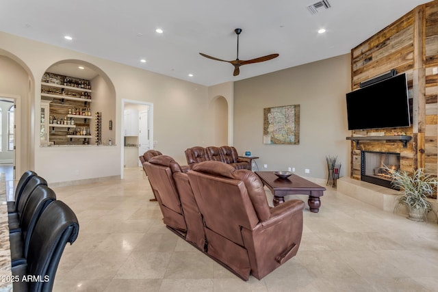 living room featuring ceiling fan, a stone fireplace, and built in features