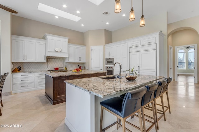 kitchen featuring sink, a breakfast bar area, white cabinetry, light stone countertops, and a kitchen island with sink