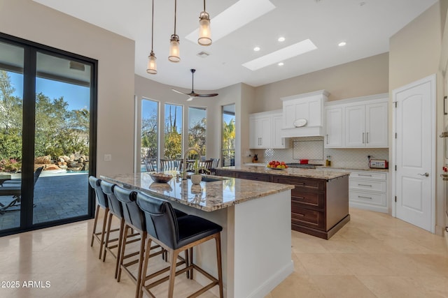 kitchen with white cabinetry, a kitchen island with sink, sink, and a skylight