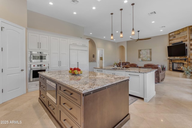 kitchen with pendant lighting, stainless steel appliances, a center island, light stone countertops, and white cabinets