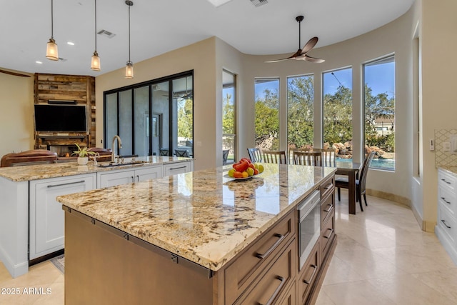 kitchen featuring light stone counters, a center island, hanging light fixtures, stainless steel microwave, and white cabinets