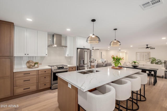 kitchen featuring stainless steel appliances, wall chimney exhaust hood, open floor plan, a sink, and light wood-style floors