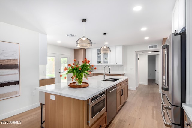 kitchen with appliances with stainless steel finishes, a sink, white cabinetry, light wood-type flooring, and baseboards